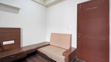Ein Zimmer mit einer Holzbank, einem kleinen Sofa, einer Holztür und einer weißen Wand mit Lichtschalter.