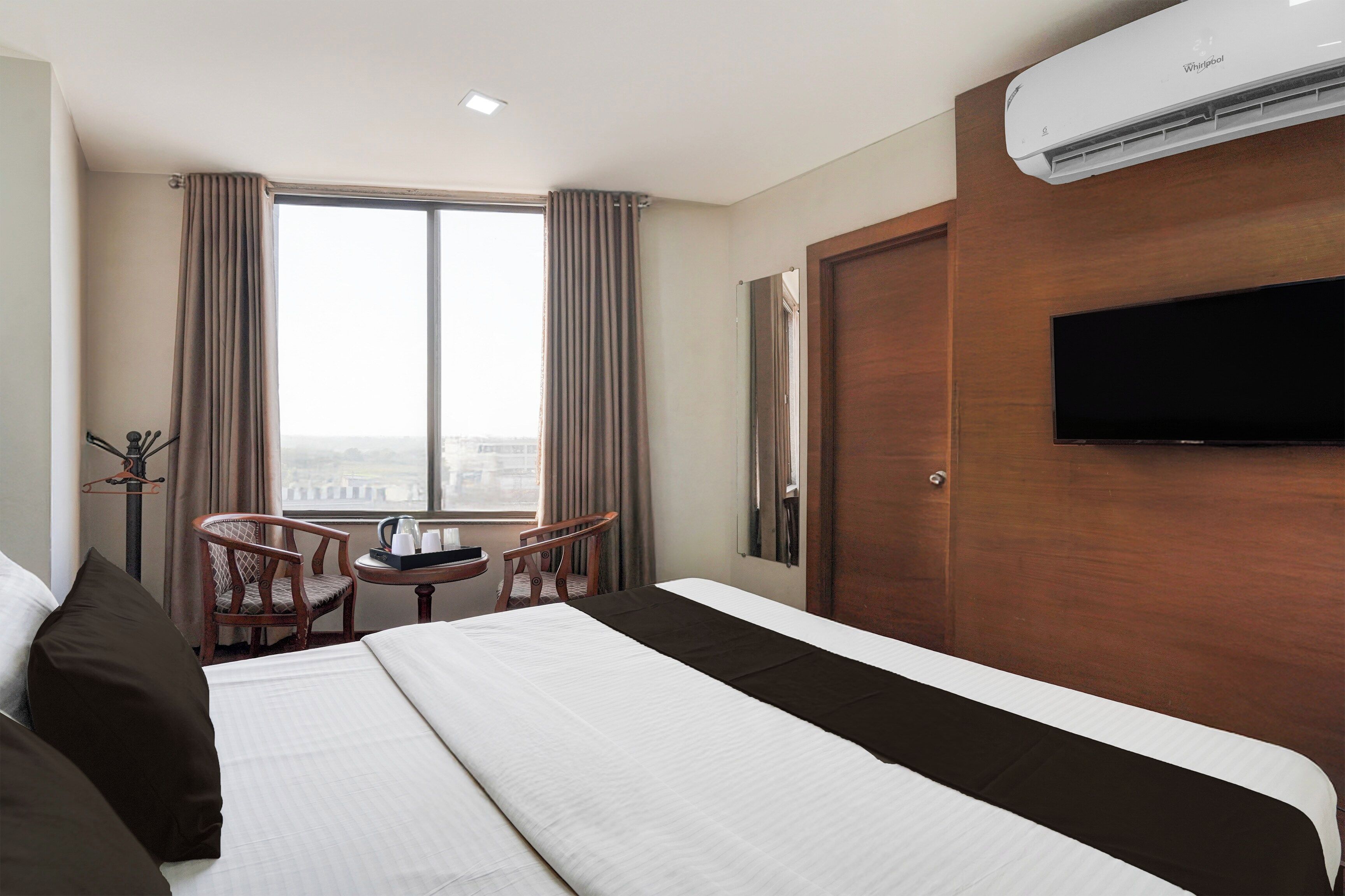 Een hotelkamer met een bed, een televisie, een raam met gordijnen en uitzicht op de stad.