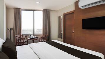 Een hotelkamer met een bed, een televisie, een raam met gordijnen en uitzicht op de stad.