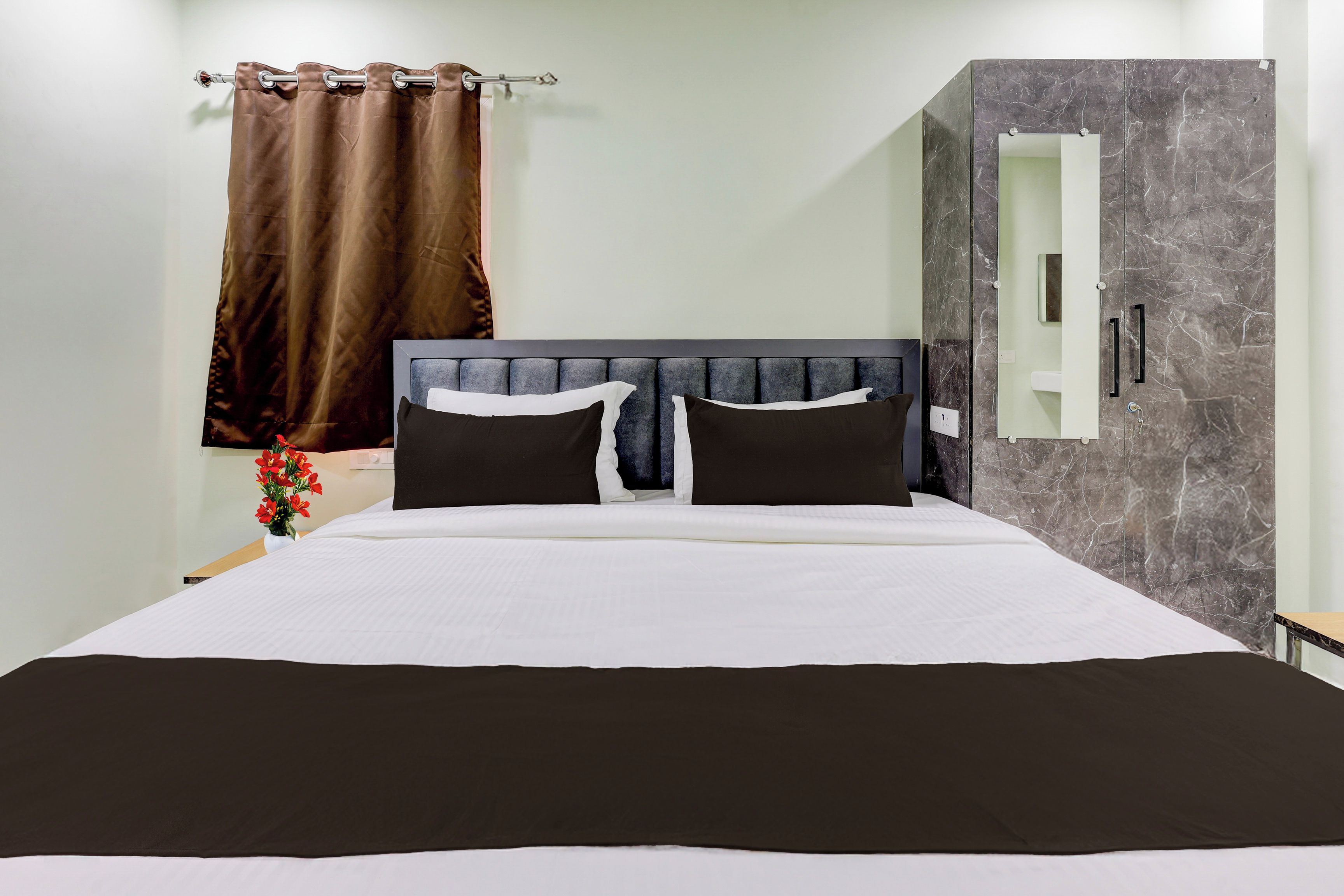 A hotel room with a bed, a nightstand, a mirror, and a curtain.