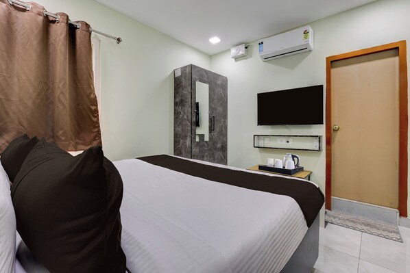 A hotel room with a bed, a television, an air conditioning unit, a mirror, and a door.