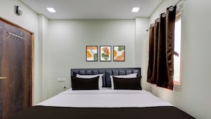 Un dormitorio con cama, una puerta de madera, una ventana con cortinas y tres cuadros en la pared.