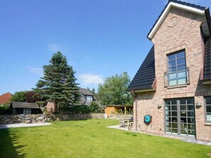 A brick house with a well-maintained lawn and a large evergreen tree. - Holiday Home Sylt Leev (Sylt)