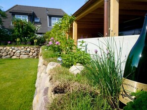 A bottle of champagne in a garden setting with a stone wall, grass, and a wooden structure in the background. - Holiday Home Sylt Leev (Sylt)