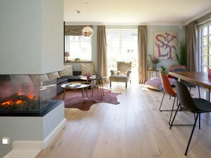A modern living room with a fireplace, a dining area, and a large window with curtains. - Holiday Home Sylt Leev (Sylt)