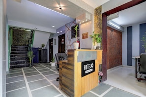 Uma área de recepção de hotel com balcão de madeira, escada e parede com textura.