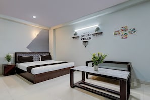 Quarto moderno com cama, mesas de cabeceira, prateleira na parede com plantas e uma frase motivacional.