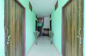 A corridor with two wooden doors on either side, leading to a room with a tiled floor and a small staircase. - Super Hotel O Dadri Main Road Greater (Greater Noida)
