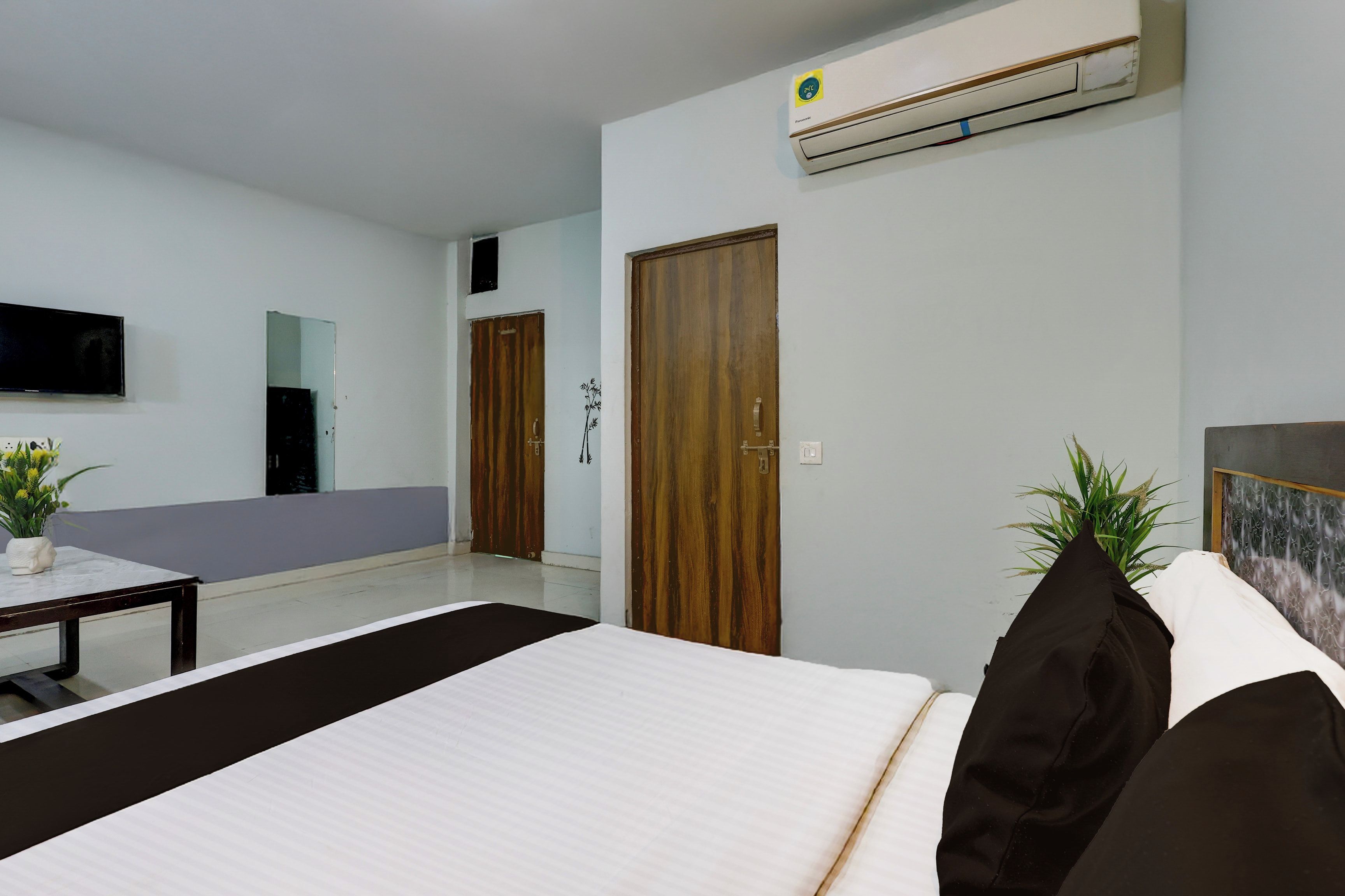 A hotel room with a bed, a TV mounted on the wall, an air conditioning unit, and a wooden door.