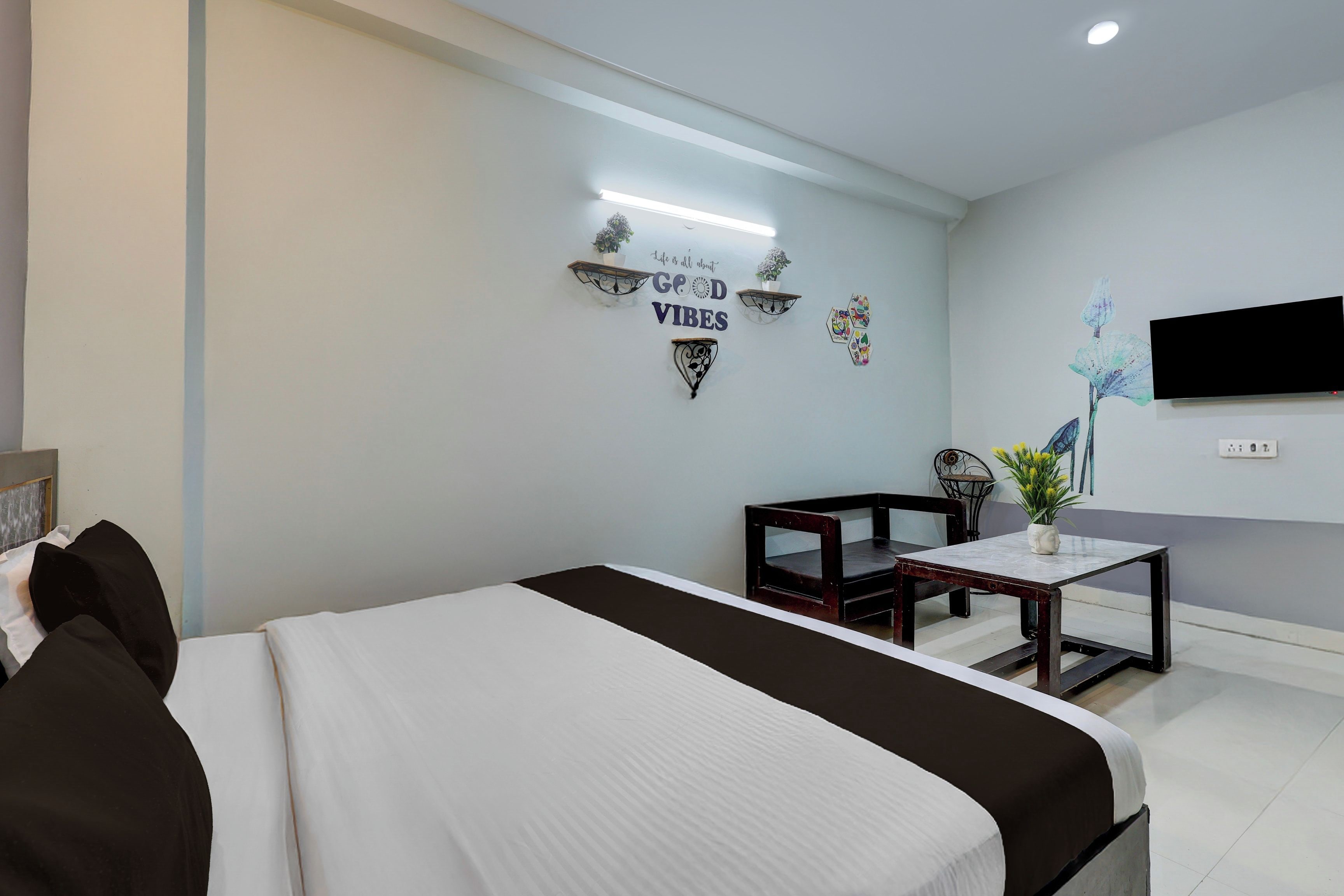 Habitación de hotel con cama, una mesita, una silla, televisor montado en la pared y decoración en la pared.