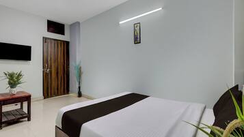 A hotel room with a bed, a small table with a plant, a door, and a wall-mounted TV.