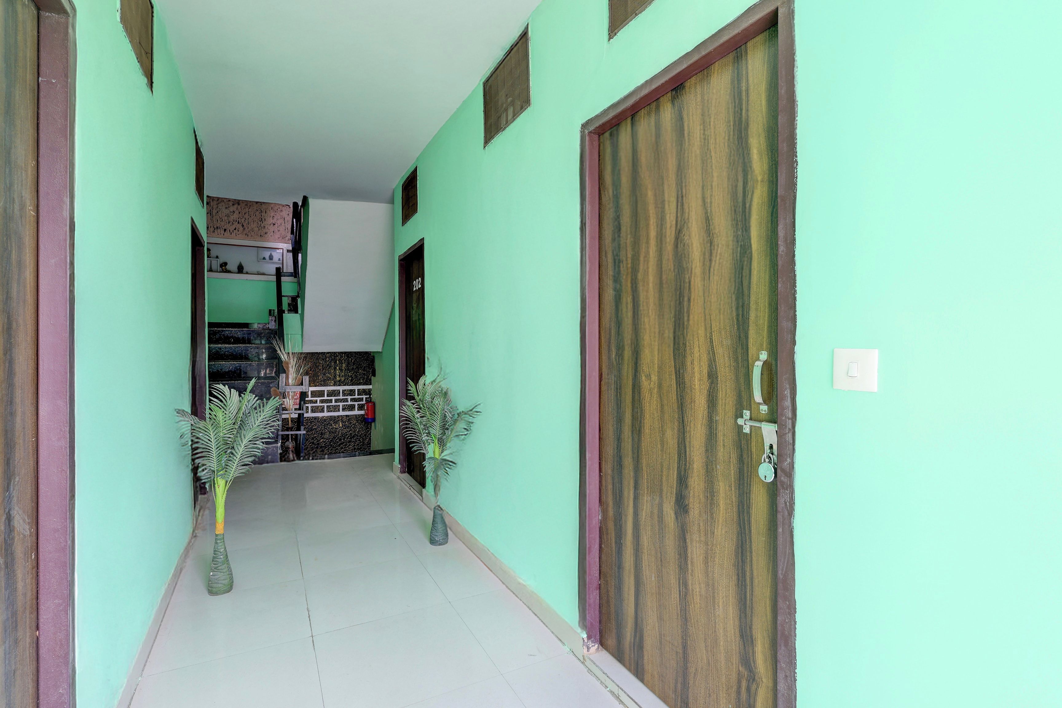 A hallway with a tiled floor, a wooden door, and a staircase leading to an upper level.