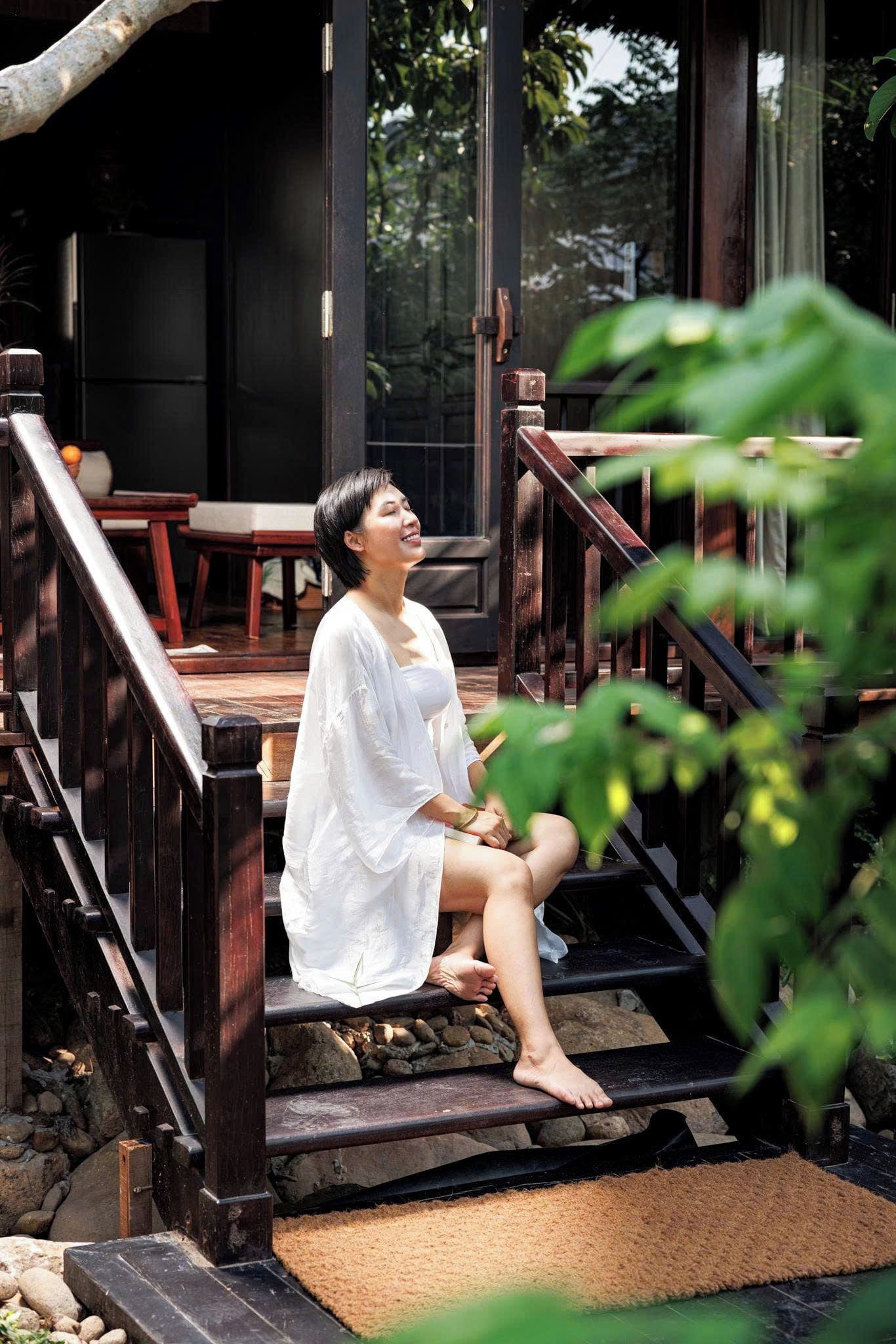 A person sitting on outdoor wooden steps with a view of a building and greenery in the background.
