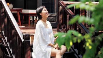 A person sitting on outdoor wooden steps with a view of a building and greenery in the background.