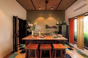A kitchen with a central island, wooden stools, a refrigerator, and a window with curtains.