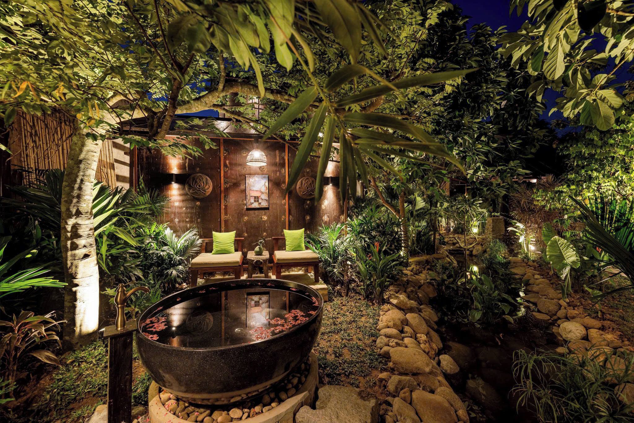 A hot tub surrounded by rocks and plants, with a wooden structure in the background.