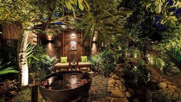 A hot tub surrounded by rocks and plants, with a wooden structure in the background.