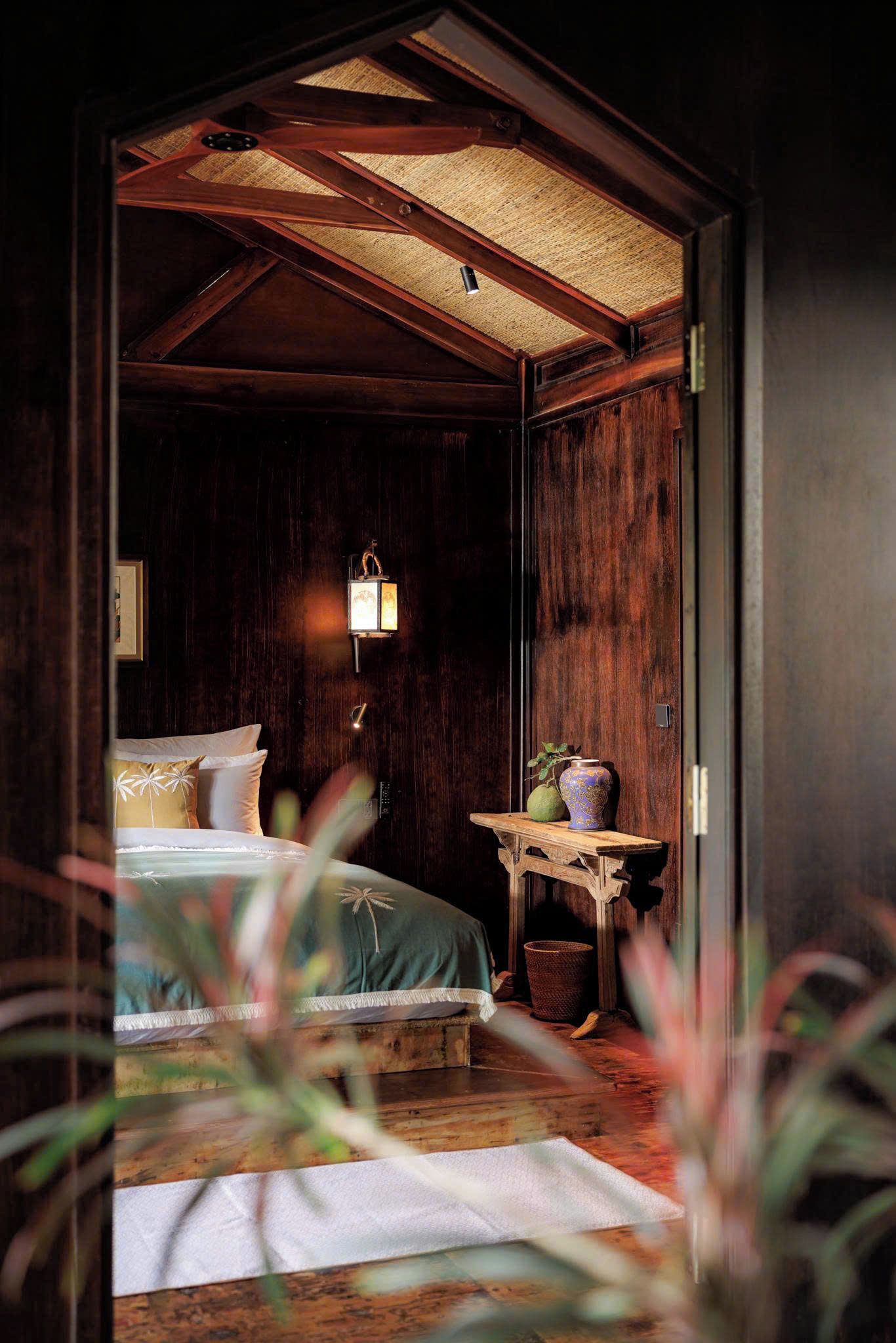 A room with a bed, a nightstand, a wall-mounted lamp, and a small table with a vase.