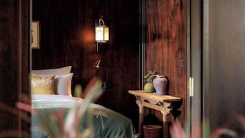 A room with a bed, a nightstand, a wall-mounted lamp, and a small table with a vase.