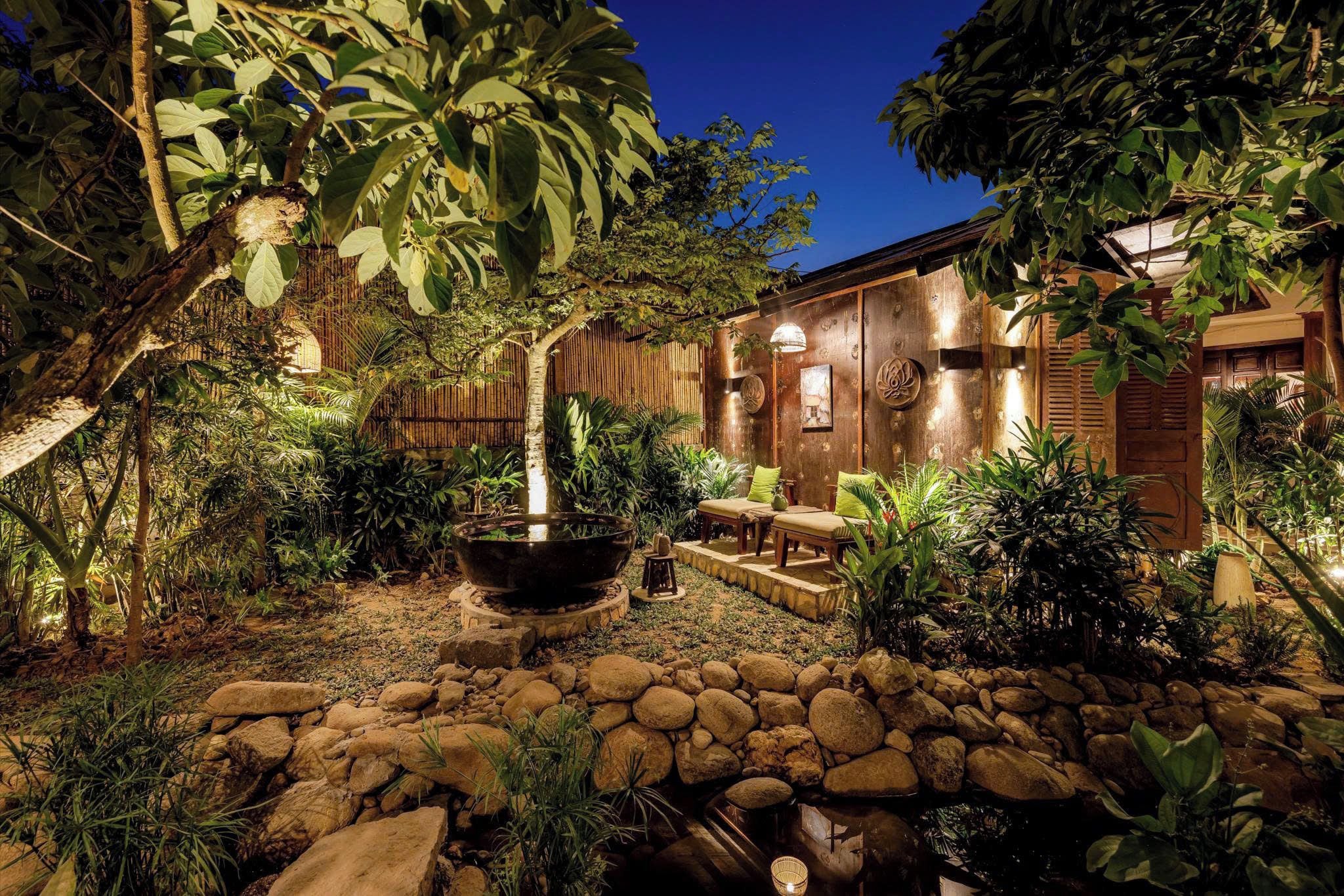 Un jardín bien cuidado con un camino de piedra, una maceta grande y una estructura de madera con una zona de estar.