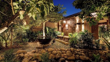 A well-maintained garden with a stone pathway, a large planter, and a wooden structure with a seating area.