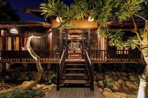 A wooden staircase leading to a building with a thatched roof and a wooden railing.