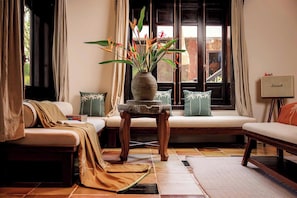 A living room with a sofa, a coffee table with a plant, and a window with curtains.