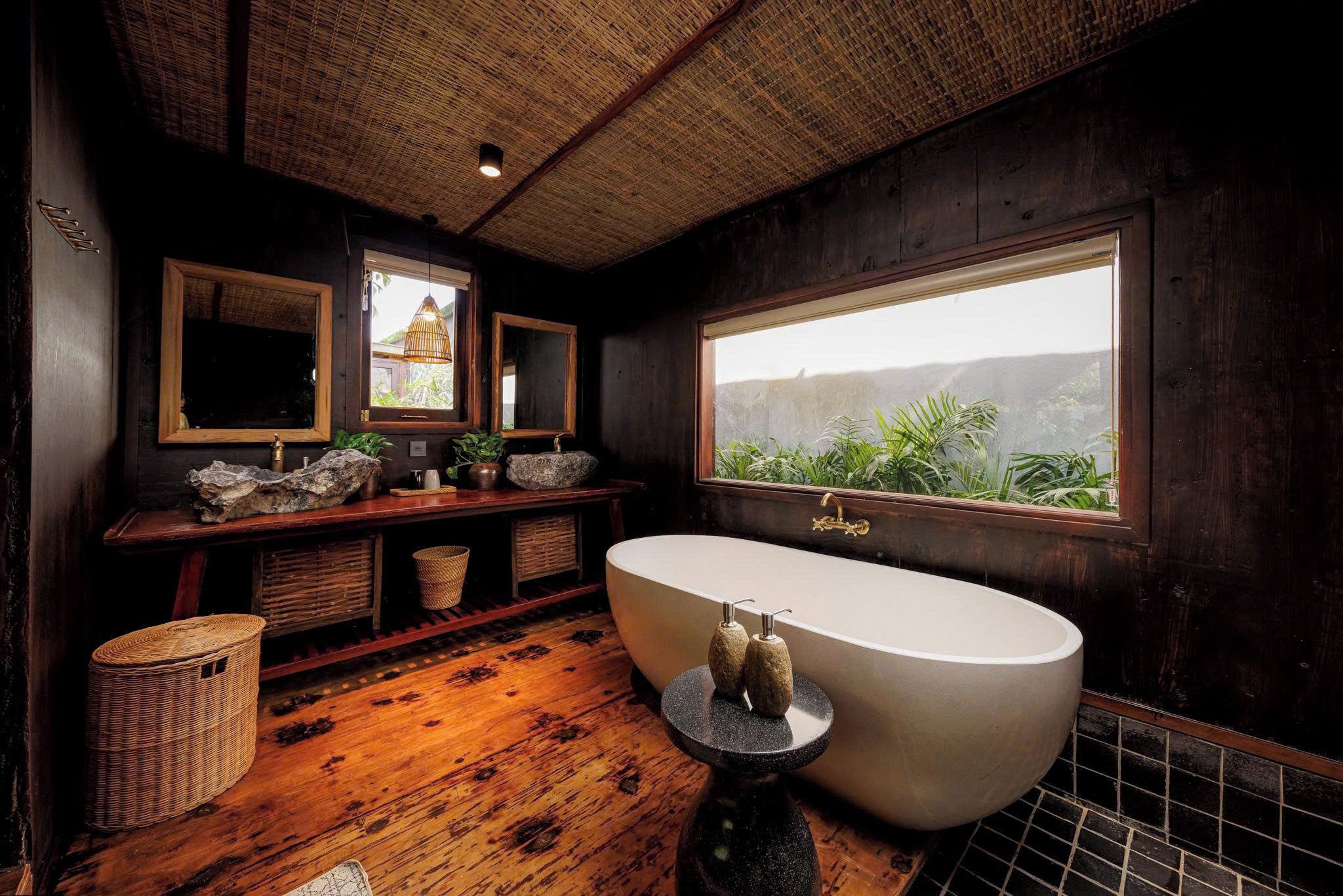 Un baño con una bañera grande, piso de madera, un ventanal con vistas y techo tejido.
