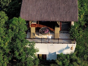 A thatched-roof structure with a circular water feature and a balcony.