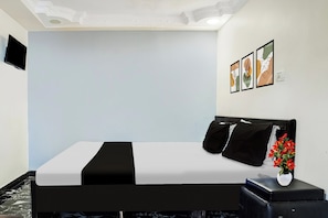Een hotelkamer met een bed, een flatscreen televisie aan de muur en een kleine tafel met een bloevas.