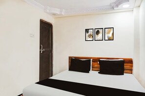 Een slaapkamer met een bed, een houten hoofdbord, een donkere deur en drie kunstwerken in lijsten aan de muur.