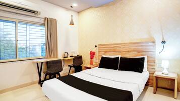 A hotel room with a bed, a desk, a chair, a nightstand, a lamp, and a window with curtains.