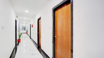A hotel corridor with a marble floor, wooden doors, and potted plants.