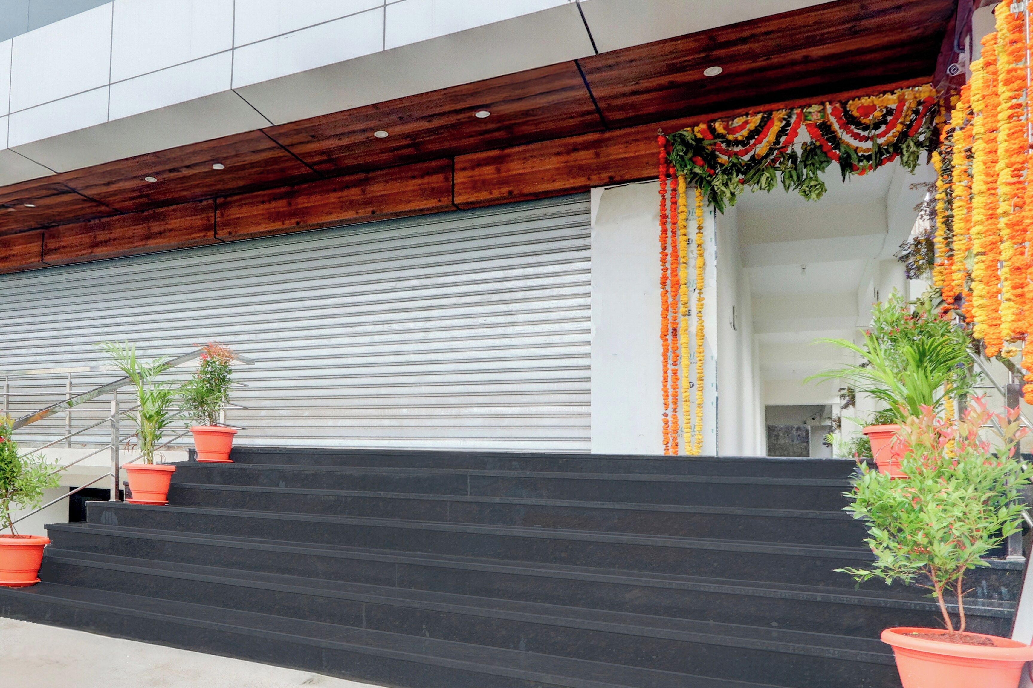 A building entrance with a set of stairs leading up to a closed garage door. There are potted plants on the steps.