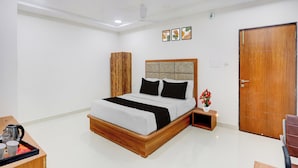 Una habitación de hotel con cama, un armario de madera, una mesita de noche con hervidor y una puerta.
