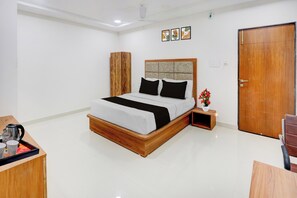 Une chambre d’hôtel avec un lit, une armoire en bois, une table de chevet avec une bouilloire et une porte.