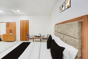 Une chambre d’hôtel comprenant un lit, une armoire en bois, un bureau avec une chaise et une étagère fixée au mur.