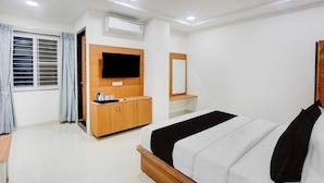 Habitación de hotel con cama, televisión montada en la pared, aparador de madera y ventana con cortinas.