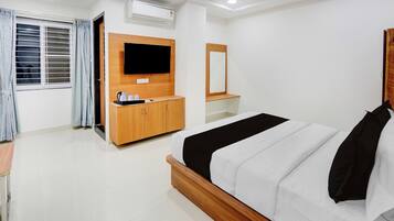 A hotel room with a bed, a TV mounted on the wall, a wooden cabinet, and a window with curtains.
