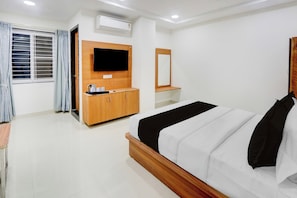 Une chambre d’hôtel avec un lit, un téléviseur fixé au mur, une armoire en bois et une fenêtre avec des rideaux.