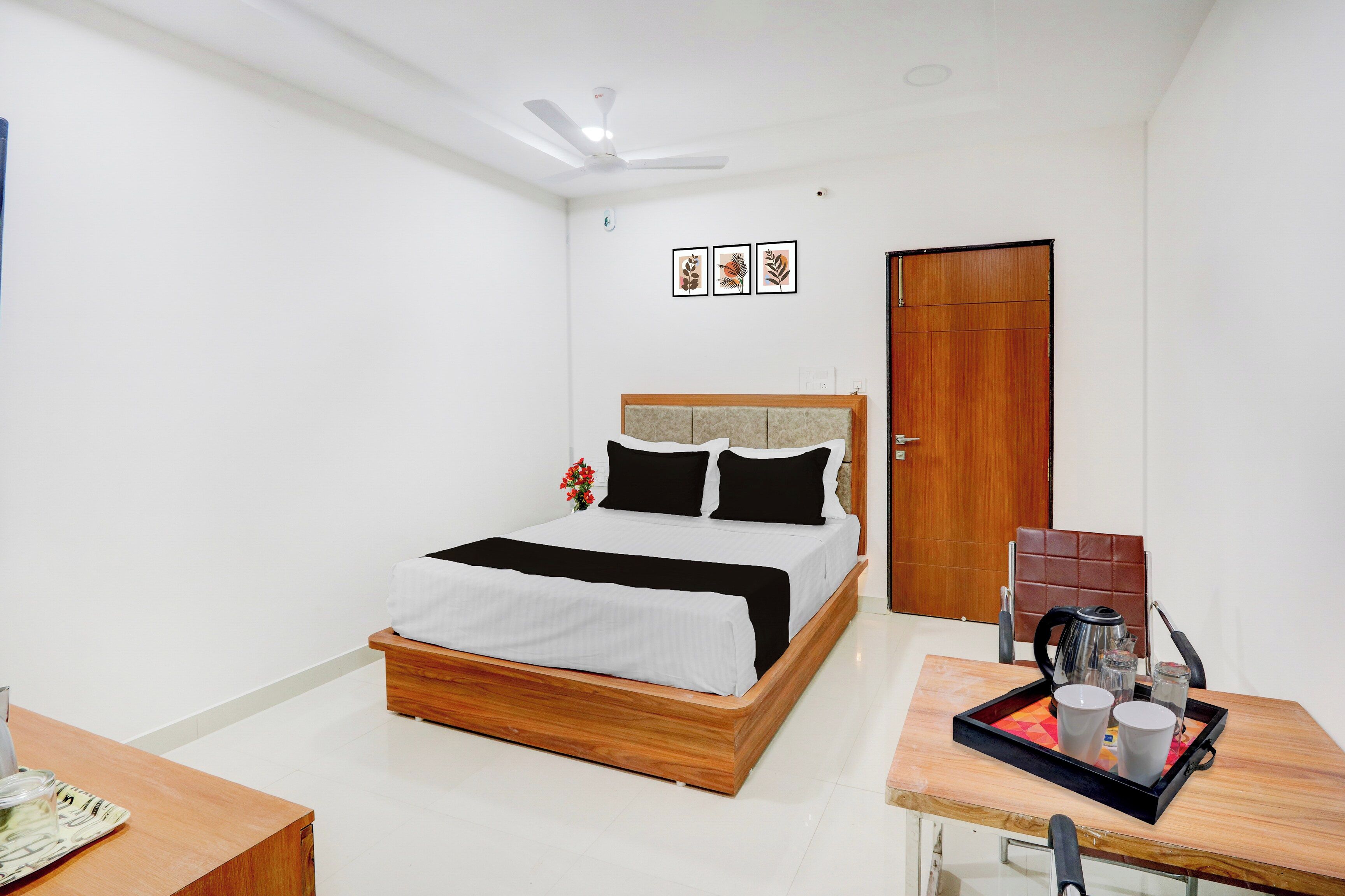 Un dormitorio con cama, mesita de noche con bandeja, puerta y ventilador de techo.