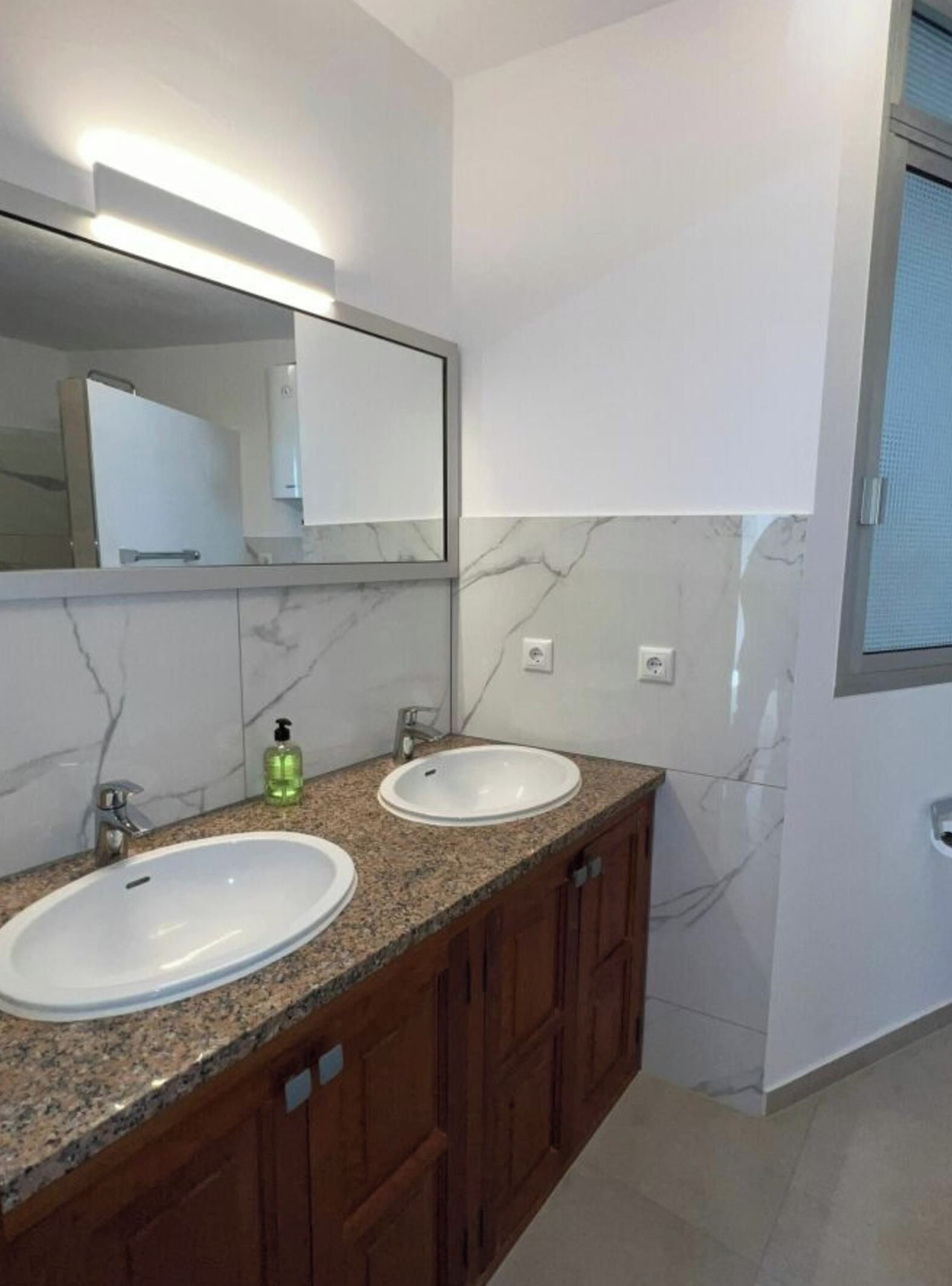 Un baño con dos lavamanos, un espejo y una ventana.