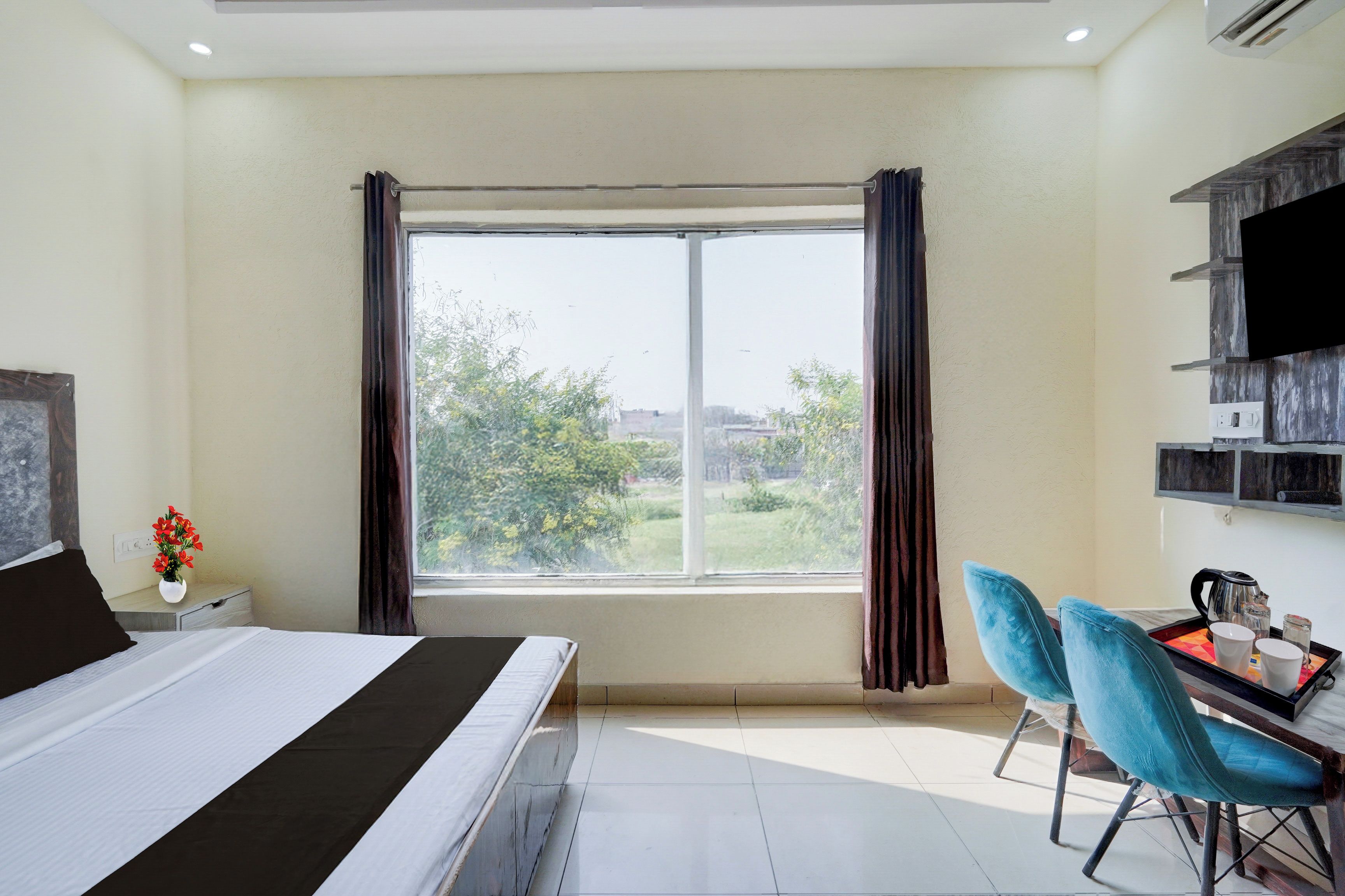 Une chambre d’hôtel comprenant un lit, un bureau avec deux chaises, une grande fenêtre avec des rideaux et un téléviseur à écran plat fixé au mur.