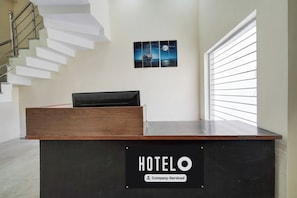 Una recepción con un cartel que dice 'HOTELO Company-Serviced' en un moderno vestíbulo de hotel con una escalera y un cuadro en la pared.