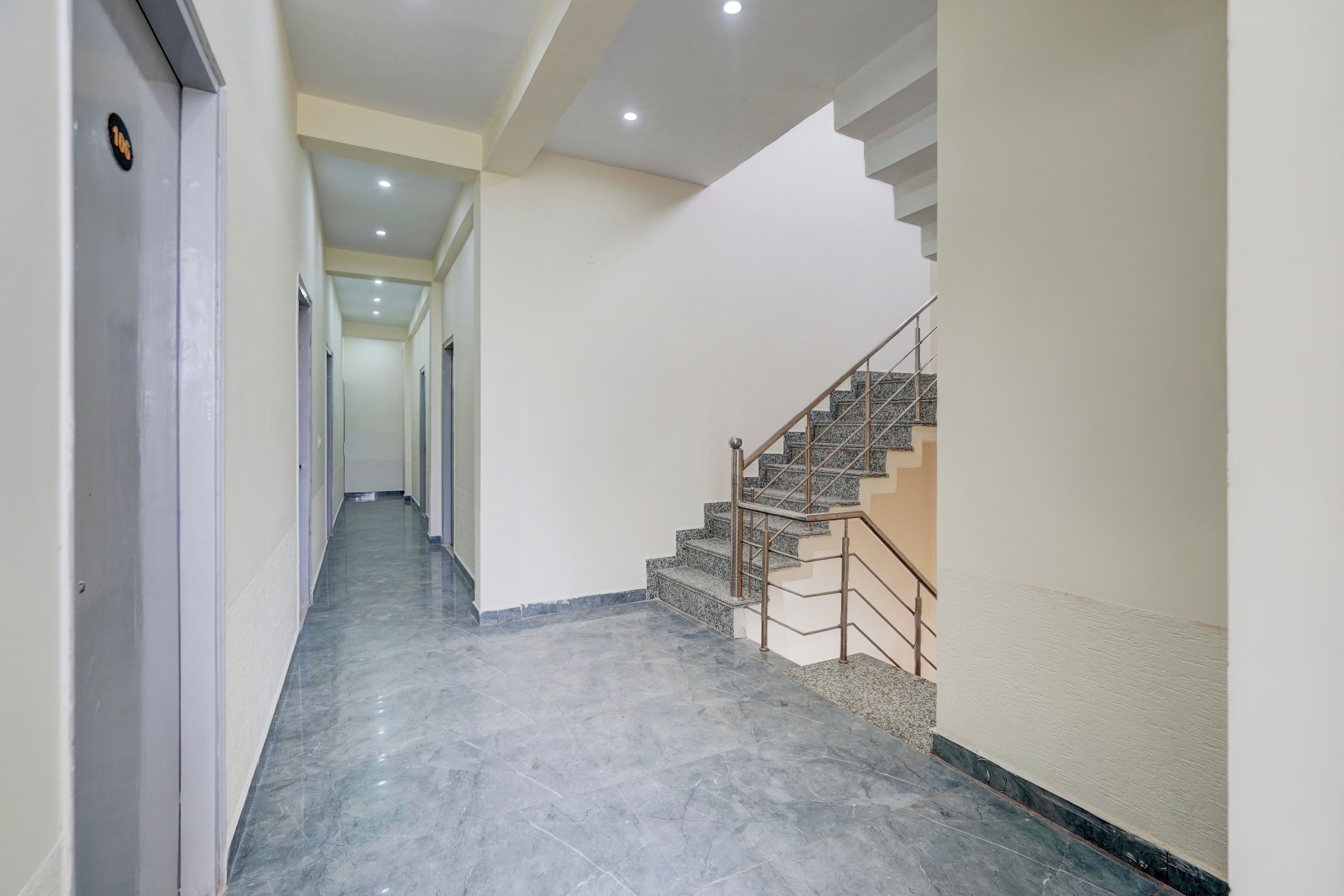 A hallway with a marble floor leading to a staircase with metal railings.