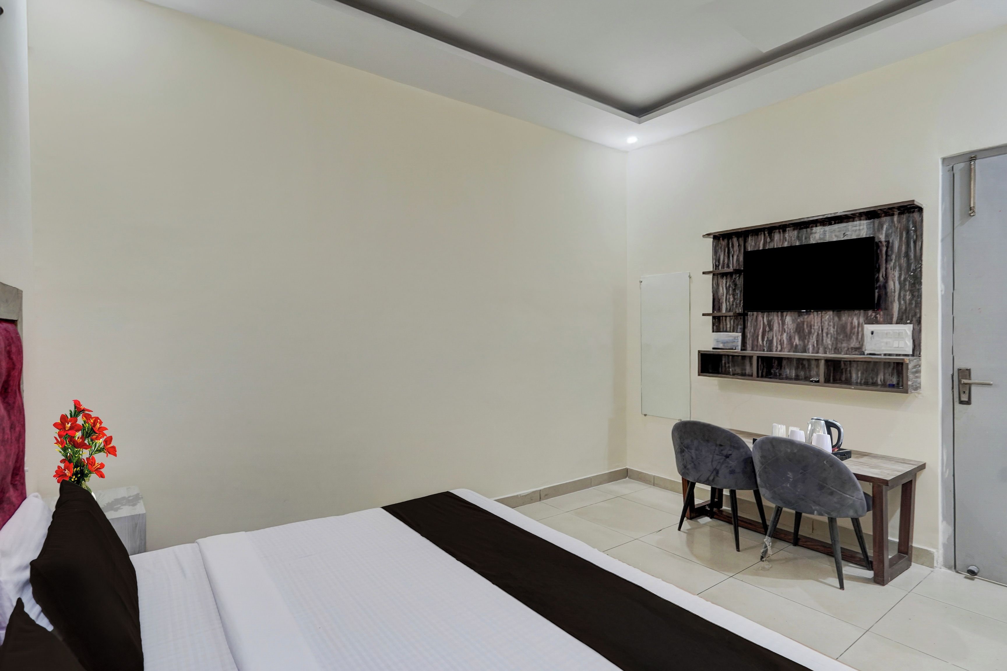 Een hotelkamer met een bed, een bureau, twee stoelen, een aan de muur bevestigde televisie en een deur.