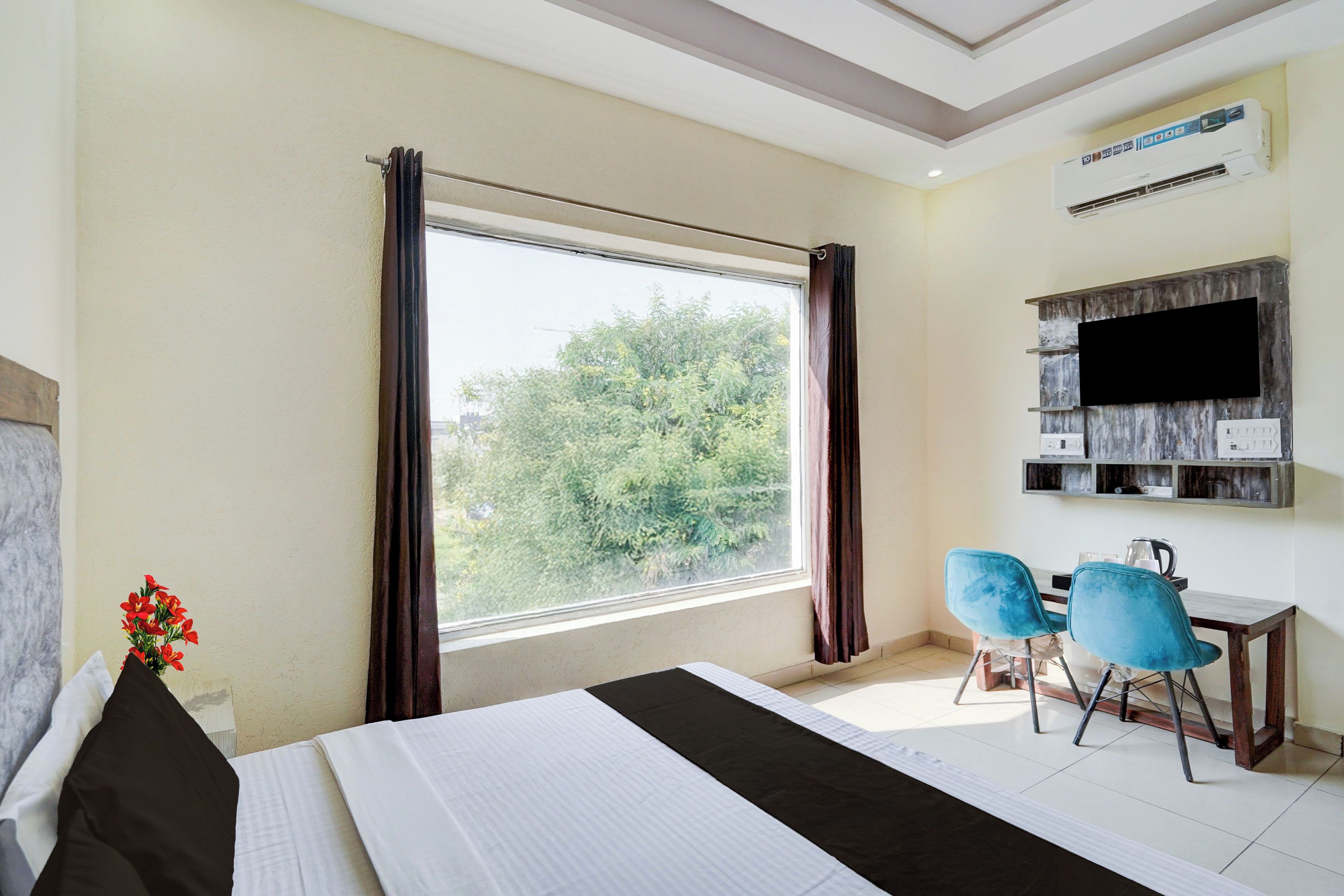 A hotel room with a bed, a desk with two chairs, a television, and a window with curtains.
