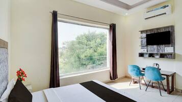 A hotel room with a bed, a desk with two chairs, a television, and a window with curtains.