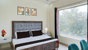 A bedroom with a bed, a nightstand, a lamp, a window with curtains, and three wall-mounted pictures.