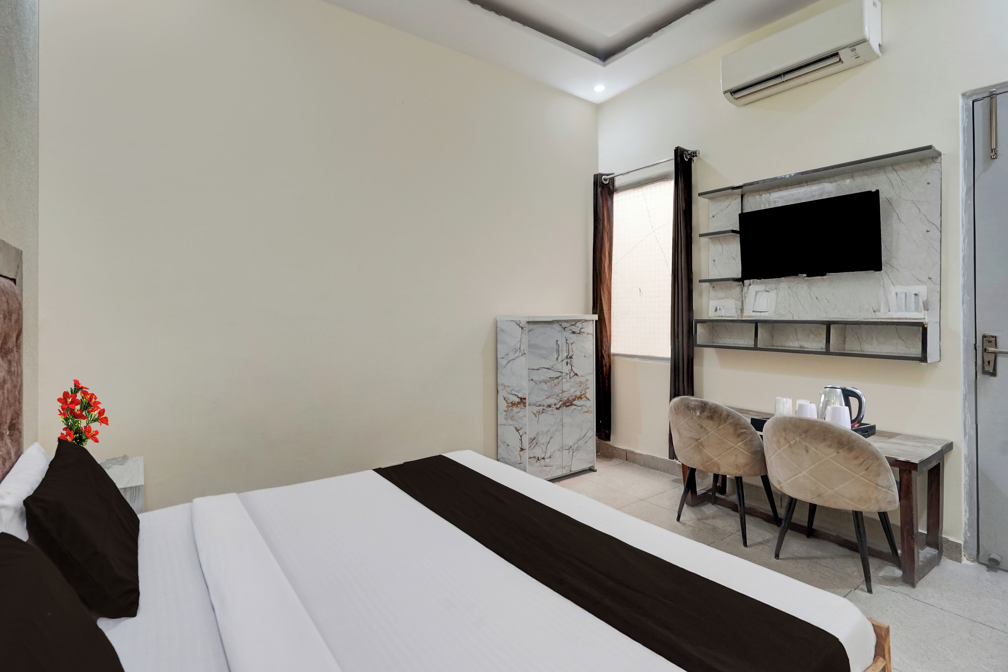 Una habitación de hotel con cama, escritorio, dos sillas, televisor y aire acondicionado.